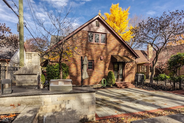 tudor-style house featuring a fireplace, a patio, and exterior kitchen