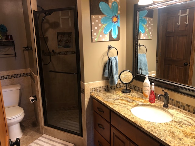 bathroom featuring toilet, large vanity, walk in shower, tile walls, and tile floors