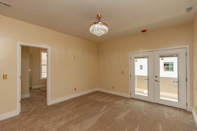 spare room featuring an inviting chandelier, light carpet, and french doors