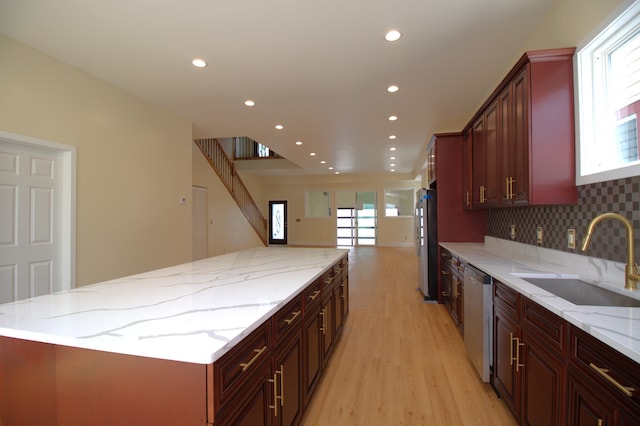 kitchen featuring appliances with stainless steel finishes, light stone counters, tasteful backsplash, light hardwood / wood-style floors, and sink