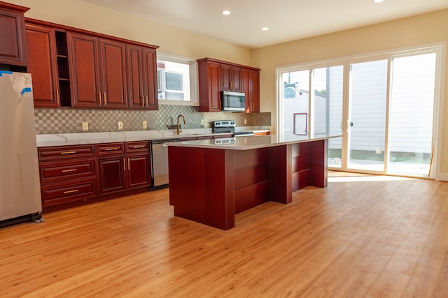 kitchen with backsplash, stainless steel appliances, a wealth of natural light, and light wood-type flooring