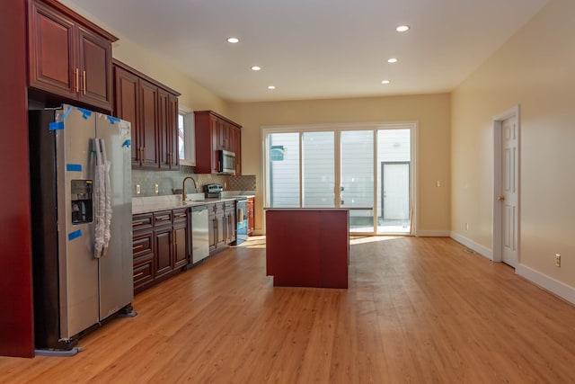 kitchen with appliances with stainless steel finishes, tasteful backsplash, a center island, light wood-type flooring, and sink