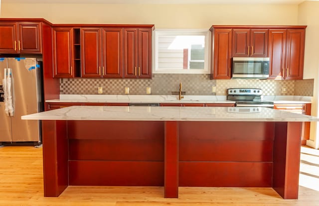 kitchen featuring light hardwood / wood-style floors, a kitchen island, light stone countertops, appliances with stainless steel finishes, and sink