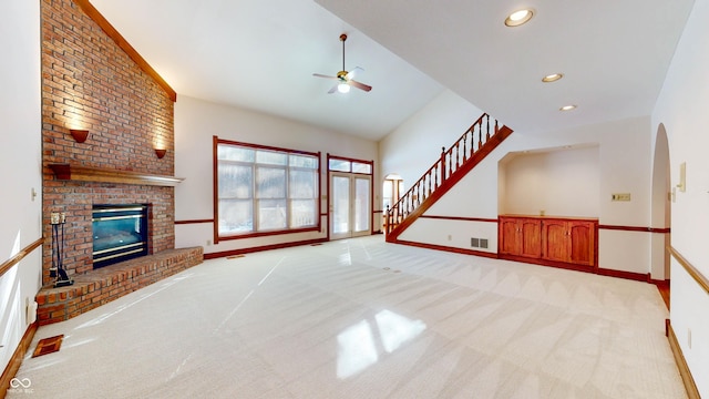 unfurnished living room with ceiling fan, lofted ceiling, a brick fireplace, and light carpet