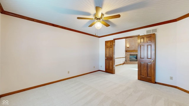 spare room with crown molding, light colored carpet, a fireplace, and ceiling fan