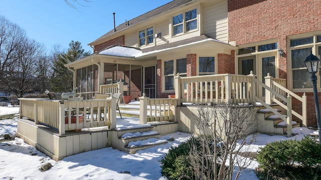 snow covered property featuring a wooden deck and a sunroom