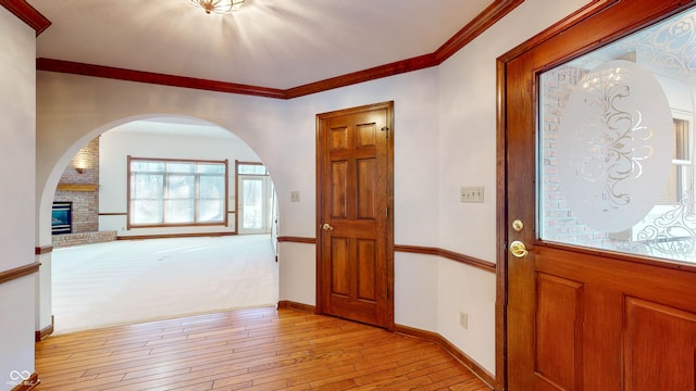 entryway with ornamental molding, a brick fireplace, and light hardwood / wood-style floors