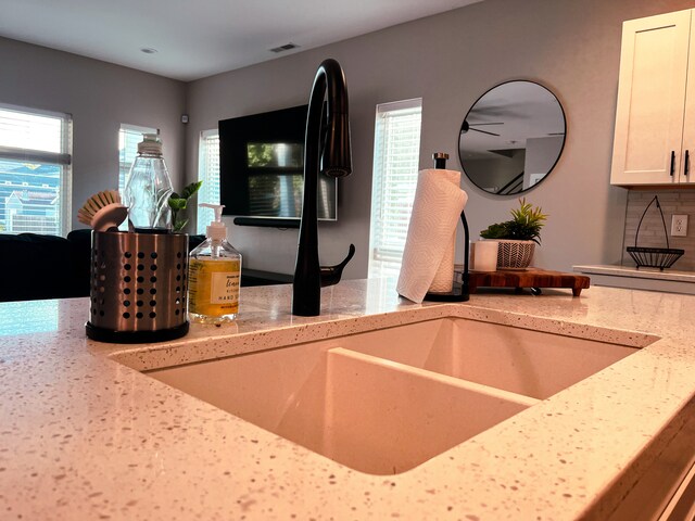 interior space featuring light stone countertops, sink, tasteful backsplash, and white cabinetry