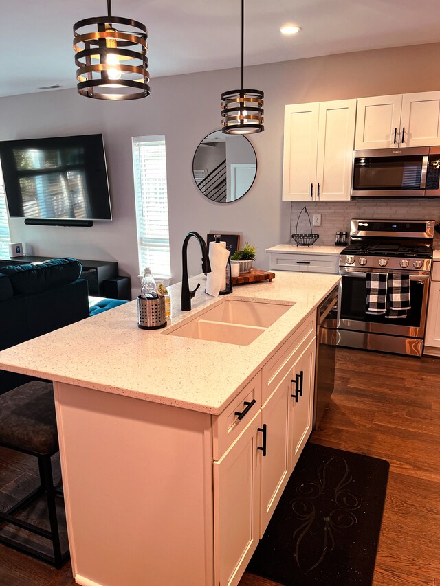 kitchen featuring dark wood-type flooring, light stone counters, an island with sink, stainless steel appliances, and sink