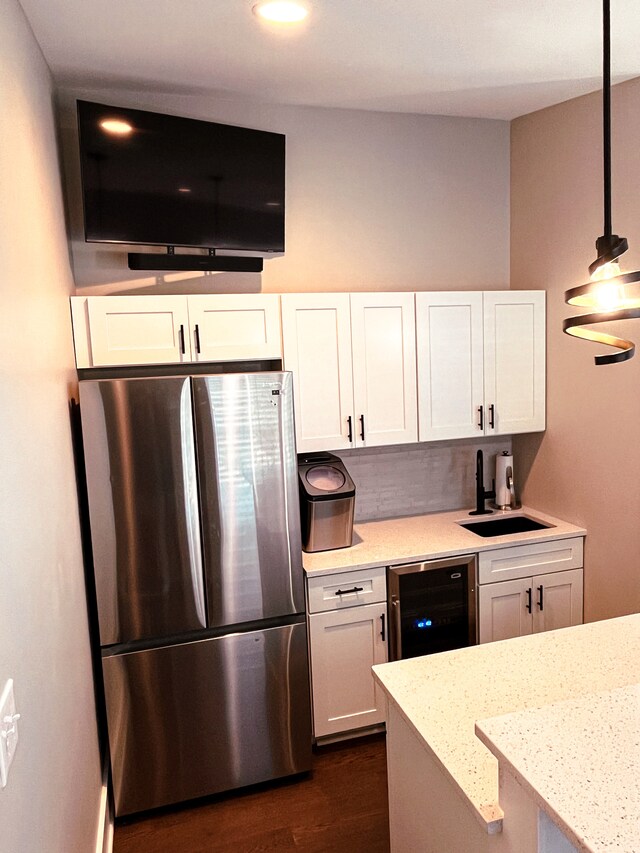 kitchen with hanging light fixtures, stainless steel refrigerator, dark wood-type flooring, light stone countertops, and white cabinets