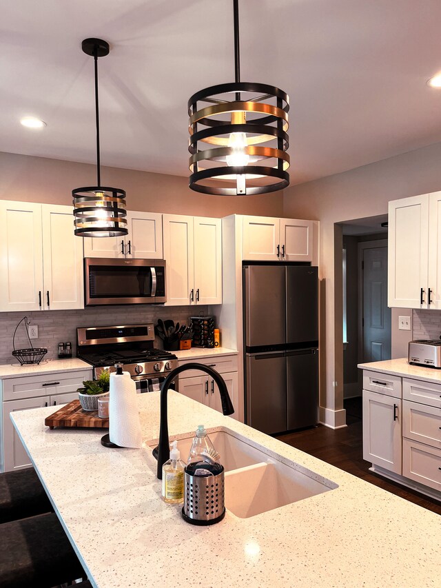 kitchen with white cabinetry, hanging light fixtures, appliances with stainless steel finishes, and light stone counters