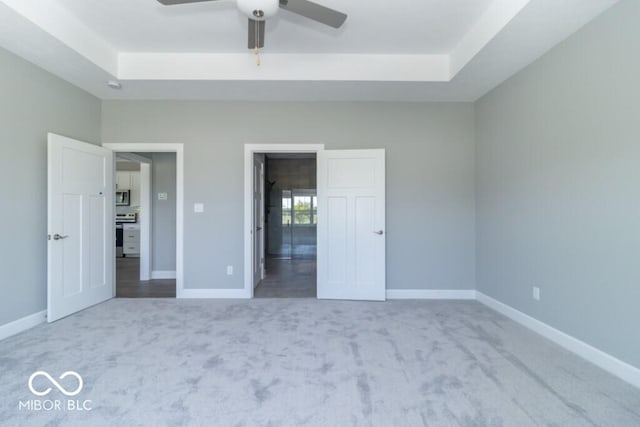 unfurnished bedroom featuring light colored carpet, ceiling fan, and a tray ceiling