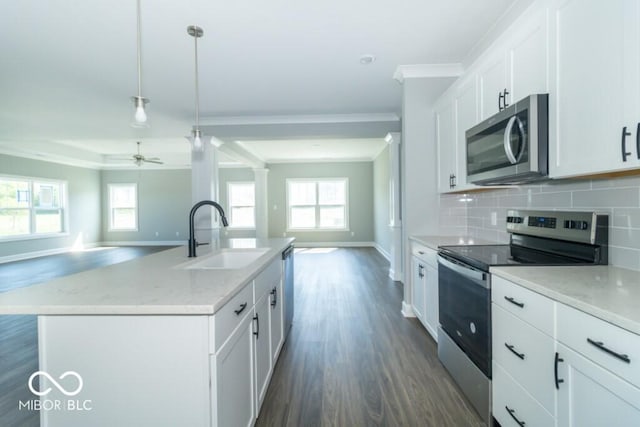 kitchen featuring appliances with stainless steel finishes, sink, white cabinets, hanging light fixtures, and a kitchen island with sink