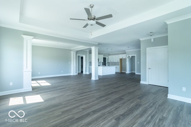 unfurnished living room with ceiling fan, a tray ceiling, decorative columns, and dark wood-type flooring