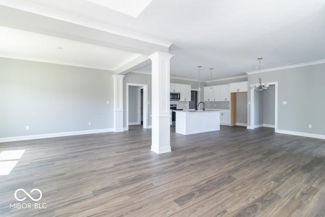 unfurnished living room featuring ornate columns, sink, ornamental molding, dark wood-type flooring, and an inviting chandelier