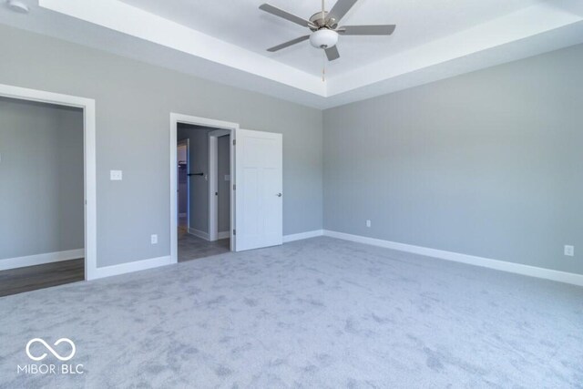 interior space featuring a raised ceiling, ceiling fan, and dark colored carpet