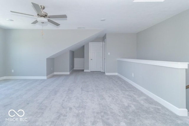 additional living space with vaulted ceiling with skylight, light colored carpet, and ceiling fan