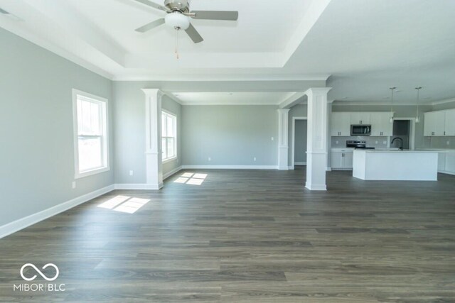 unfurnished living room featuring ceiling fan, a tray ceiling, decorative columns, and dark wood-type flooring