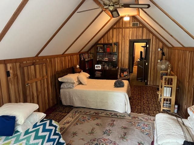 bedroom featuring wood walls, ceiling fan, and vaulted ceiling