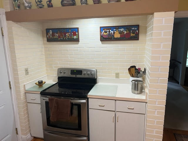 kitchen featuring brick wall, tasteful backsplash, stainless steel electric range oven, and white cabinetry