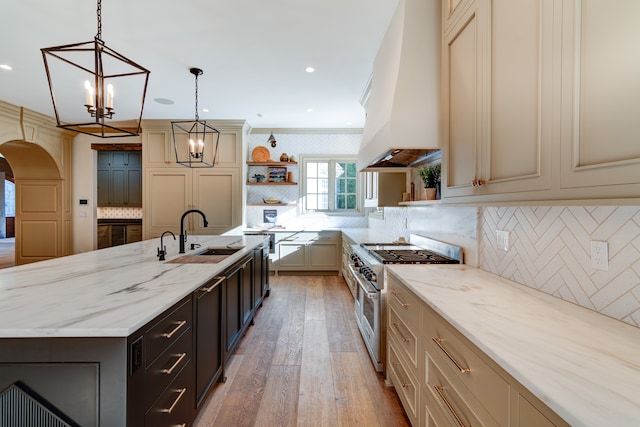 kitchen featuring double oven range, custom exhaust hood, a kitchen island with sink, backsplash, and ornamental molding