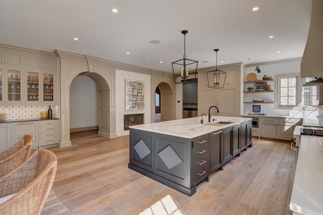 kitchen with an island with sink, light hardwood / wood-style floors, tasteful backsplash, gray cabinets, and sink