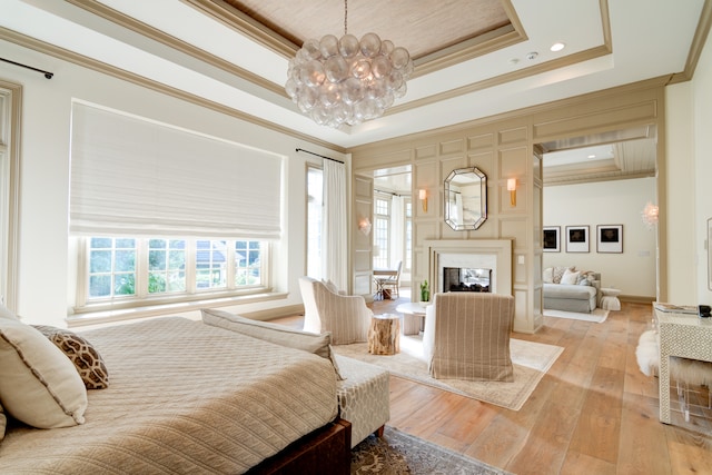 bedroom with light hardwood / wood-style flooring, a notable chandelier, ornamental molding, and a tray ceiling