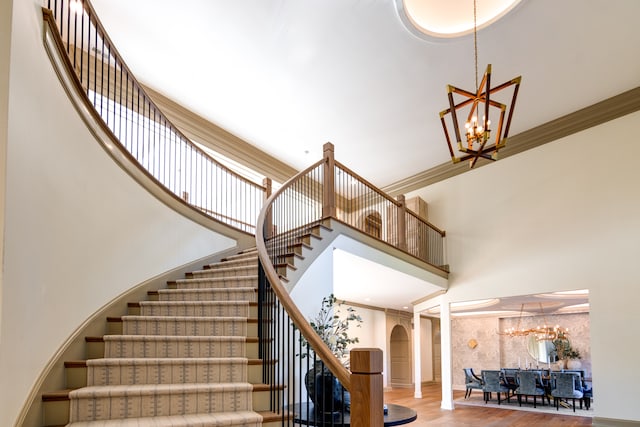 stairs featuring a towering ceiling, an inviting chandelier, ornamental molding, and light wood-type flooring