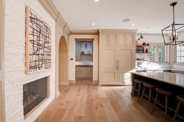 kitchen featuring tasteful backsplash, a breakfast bar area, light hardwood / wood-style flooring, pendant lighting, and ornamental molding