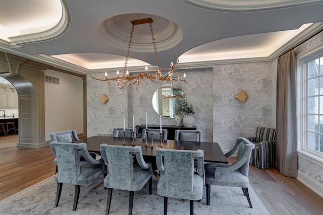 dining room featuring an inviting chandelier, light hardwood / wood-style flooring, a raised ceiling, and plenty of natural light