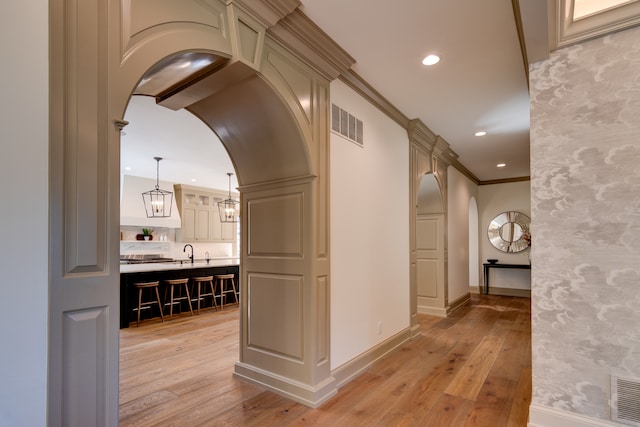 hallway with sink, ornamental molding, and light hardwood / wood-style floors