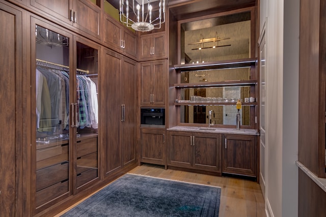 walk in closet featuring sink, a chandelier, and light hardwood / wood-style flooring