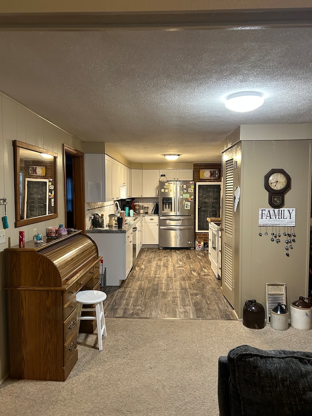 kitchen with a textured ceiling, white cabinetry, dark colored carpet, and stainless steel refrigerator with ice dispenser