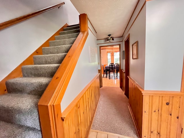 staircase featuring carpet flooring, wood walls, and a textured ceiling