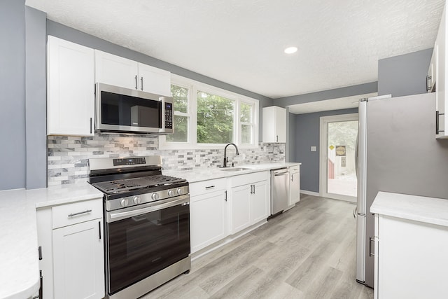 kitchen featuring light hardwood / wood-style floors, stainless steel appliances, tasteful backsplash, white cabinets, and sink