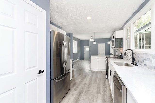 kitchen with light hardwood / wood-style floors, decorative light fixtures, appliances with stainless steel finishes, white cabinets, and sink