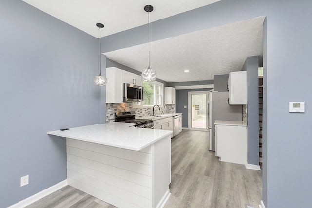 kitchen with appliances with stainless steel finishes, white cabinetry, backsplash, and light hardwood / wood-style flooring