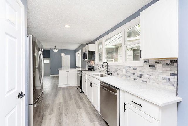 kitchen with appliances with stainless steel finishes, light hardwood / wood-style floors, white cabinets, sink, and hanging light fixtures