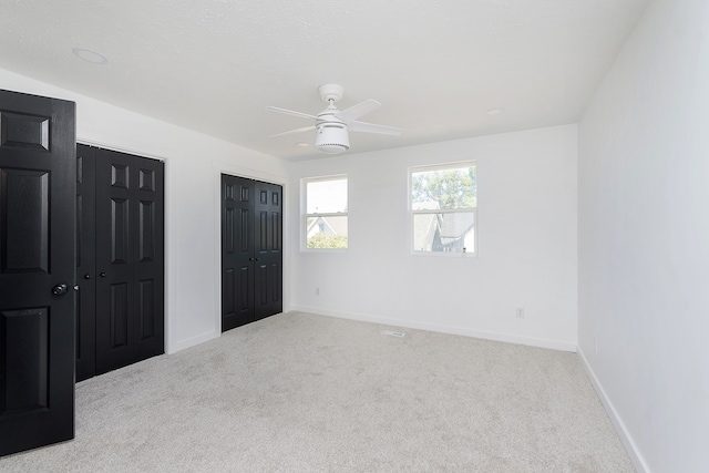 unfurnished bedroom with two closets, light colored carpet, and ceiling fan