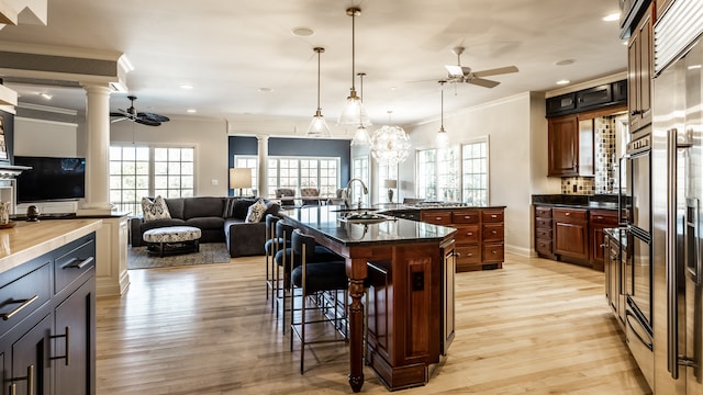 kitchen featuring a center island with sink, ceiling fan, ornate columns, and crown molding