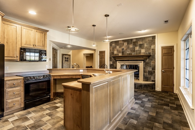 kitchen with black appliances, a fireplace, an island with sink, light brown cabinetry, and decorative light fixtures