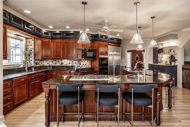 kitchen featuring a large island with sink, built in appliances, hanging light fixtures, and sink