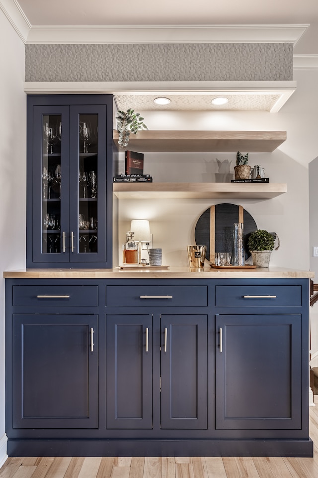 bar featuring light hardwood / wood-style floors, blue cabinets, and crown molding