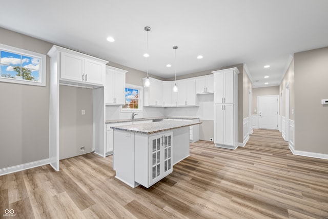 kitchen with a kitchen island, light stone countertops, pendant lighting, and white cabinets