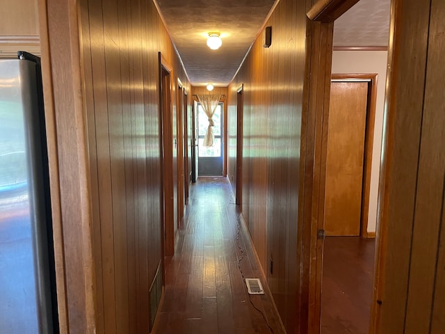 hallway with wood-type flooring, wood walls, and crown molding