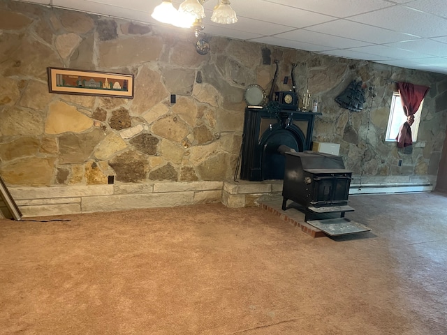 interior space featuring carpet flooring, a baseboard heating unit, a drop ceiling, and a wood stove