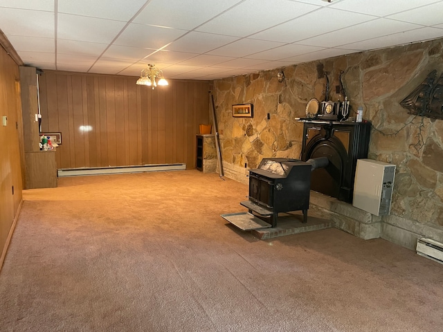 basement with an inviting chandelier, a wood stove, a paneled ceiling, carpet floors, and baseboard heating