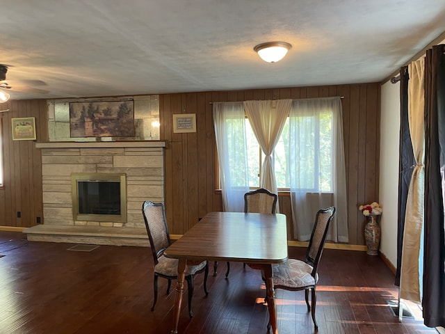 dining space featuring ceiling fan, dark hardwood / wood-style floors, wood walls, and a fireplace