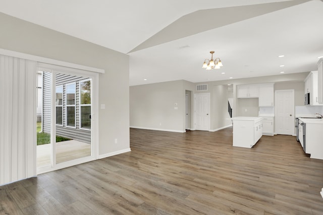 interior space featuring hanging light fixtures, hardwood / wood-style floors, vaulted ceiling, white cabinetry, and a chandelier