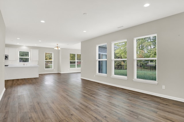 unfurnished living room featuring an inviting chandelier and dark hardwood / wood-style flooring